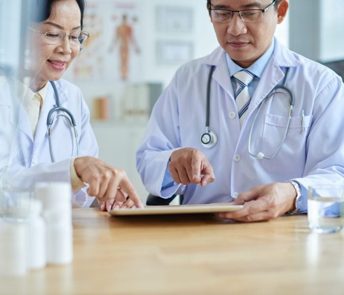 Concentrated Asian physicians discussing treatment options with help of digital tablet while having meeting in board room